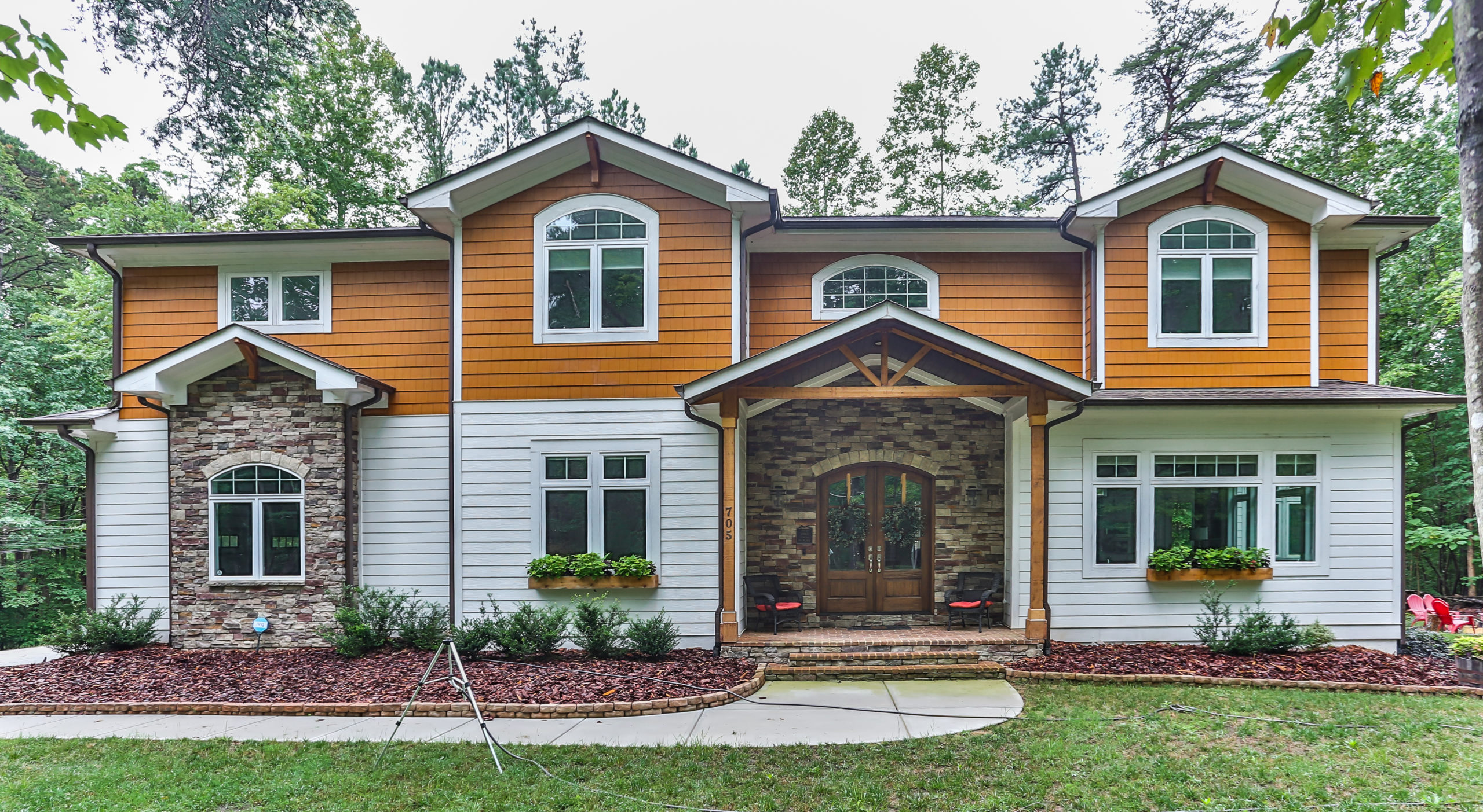Exterior view of a two-story rustic prairie-style custom home in Chapel Hill, NC, featuring stone and shake siding, arched windows, and a covered wood-beam entry.
